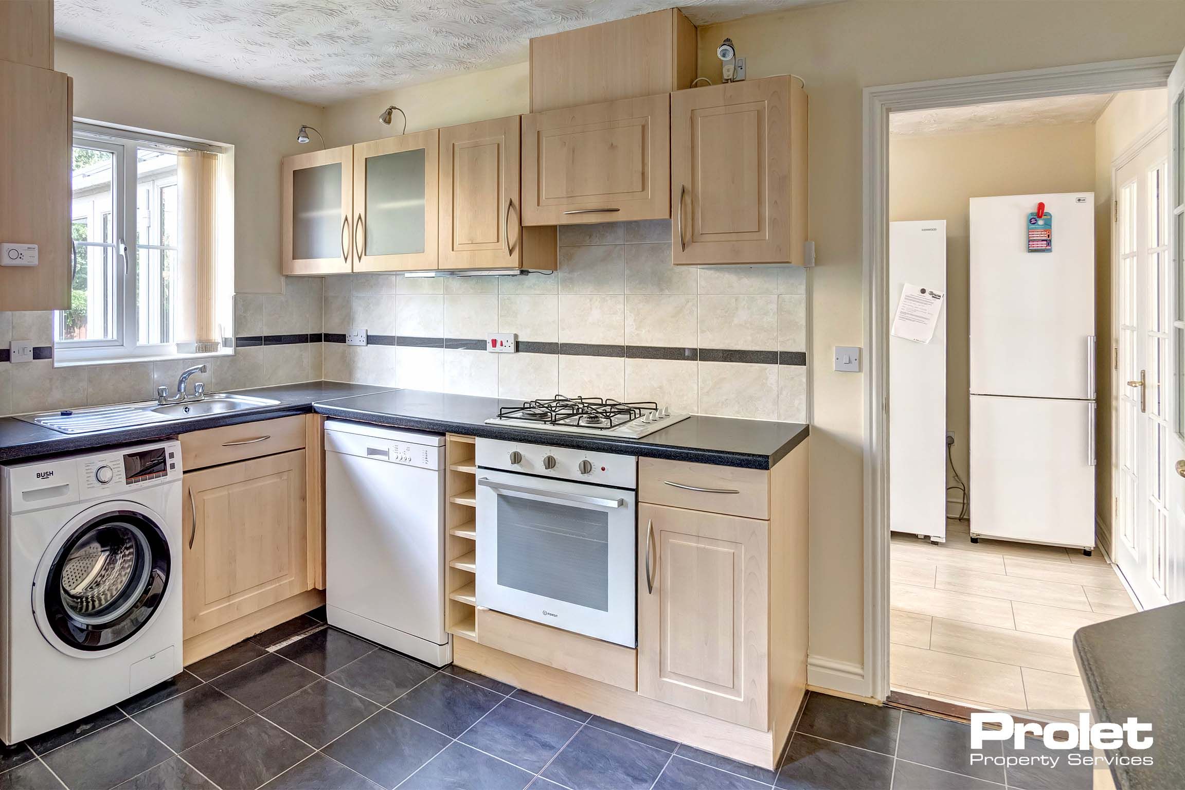 Fitted kitchen with wooden look units and oven/hob and under the counter fridge and washing machine.