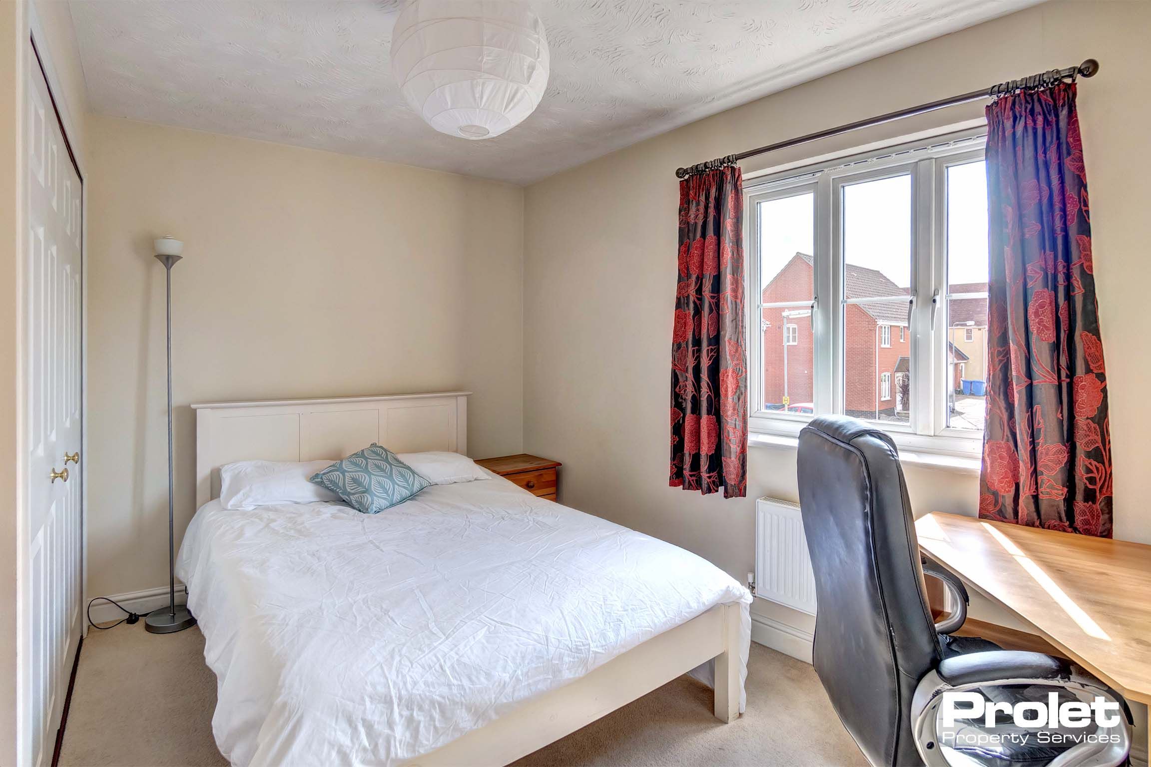 Double bedroom with built in white wardrobes and a wooden corner desk.