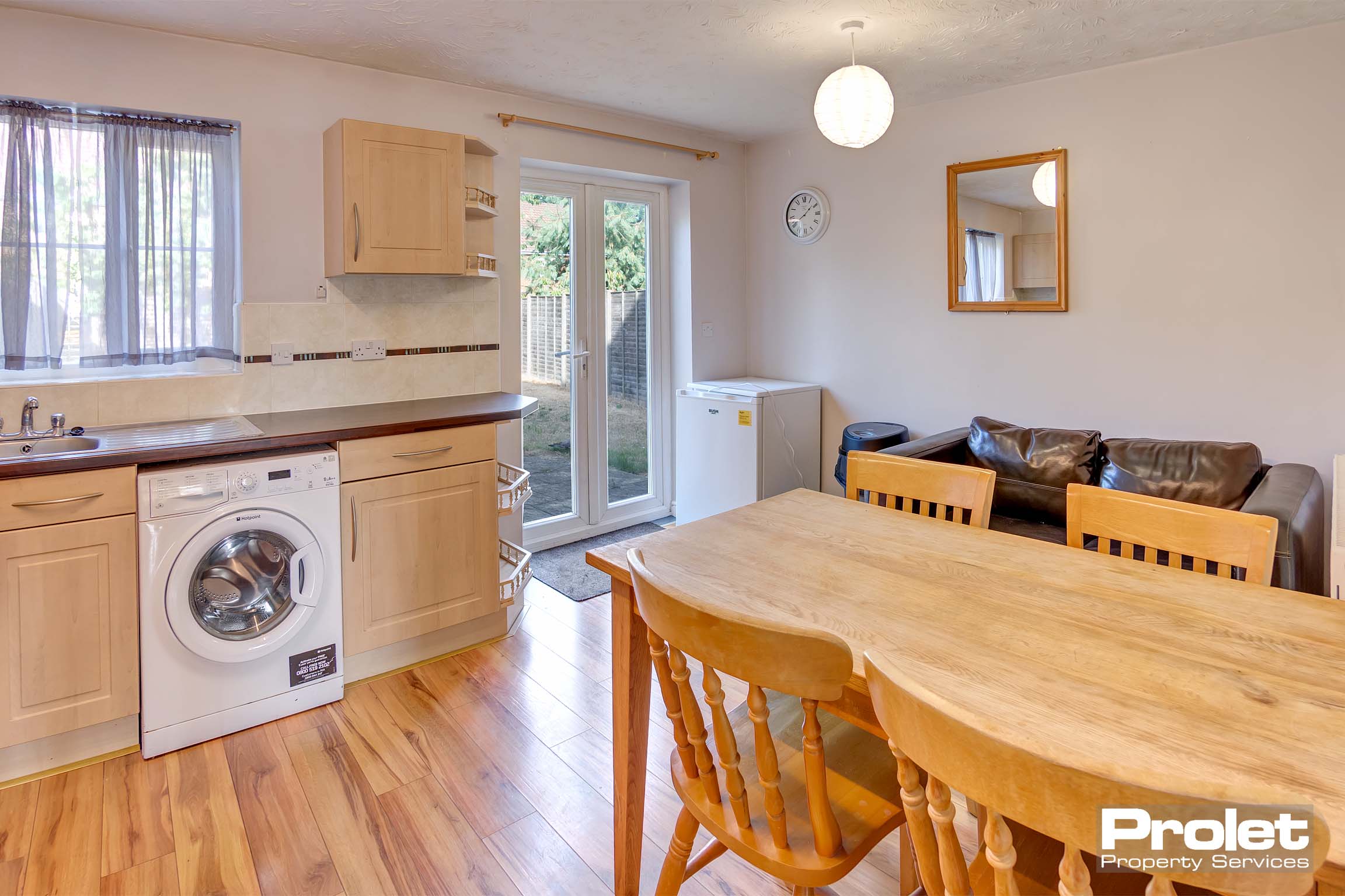 Fitted kitchen with wooden look units with under the counter washing machine. Wooden dining table and chair set and a black leather sofa.