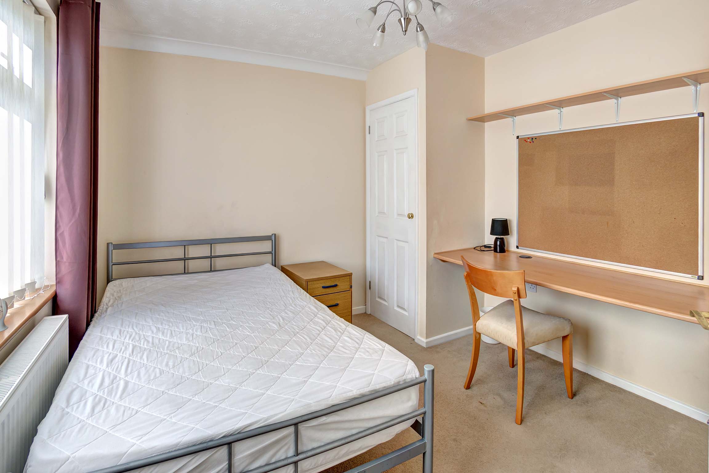 Double bedroom with metal bed frame, built in wardrobe, and a fitted desk with a cork board above.