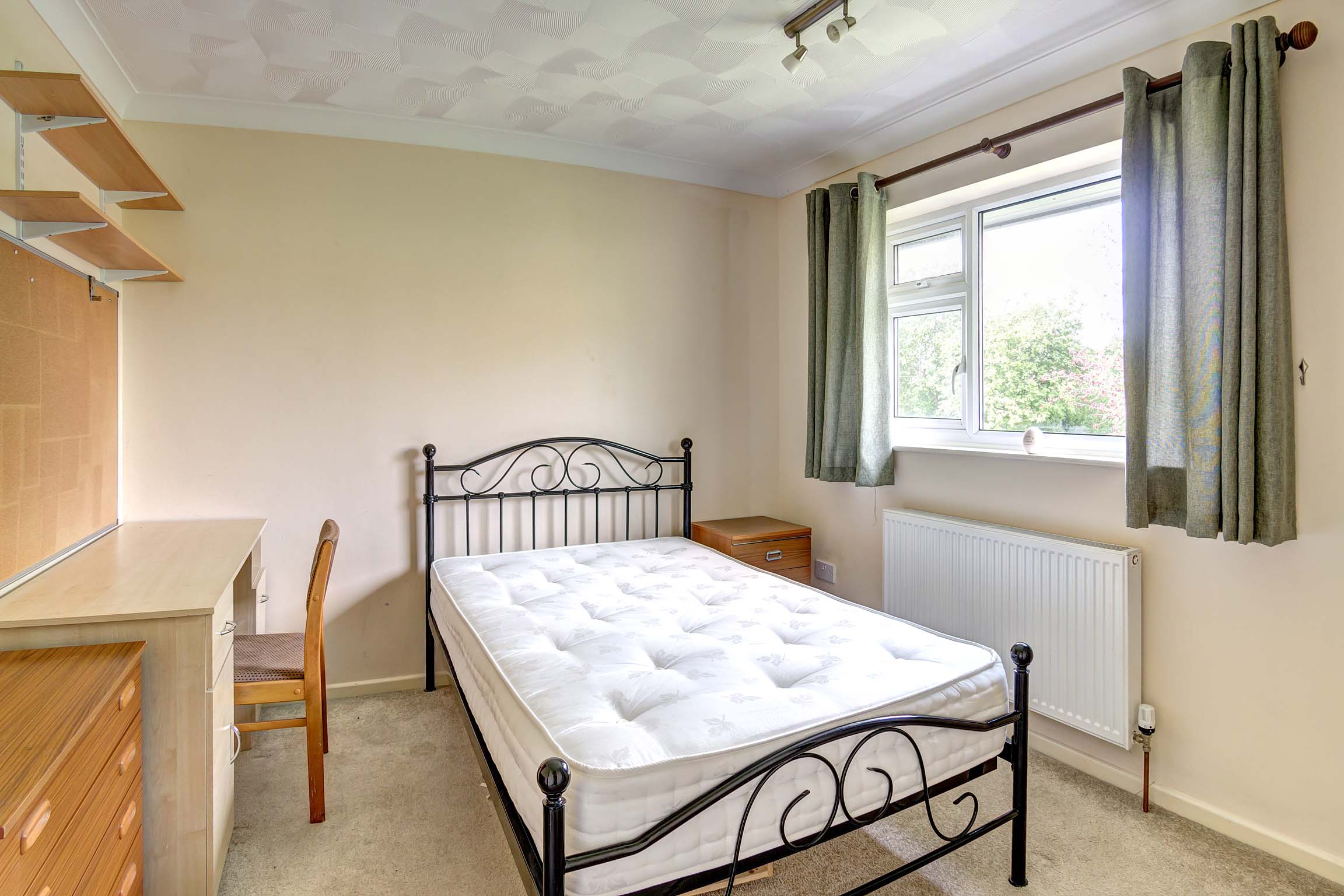 Magnolia painted bedroom with desk and chair next to a wooden set of chest of drawers.