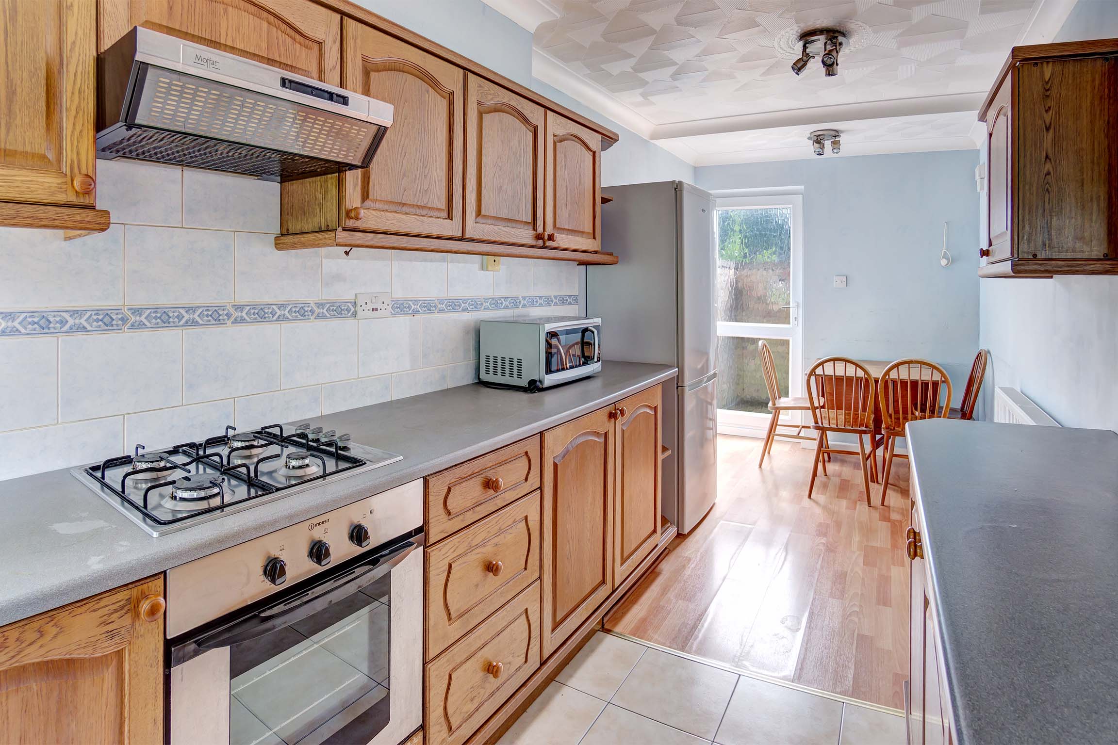 Galley style kitchen with wooden fitted kitchen. Oven and gas hob. Opens into dining area with wooden dining table and chairs.