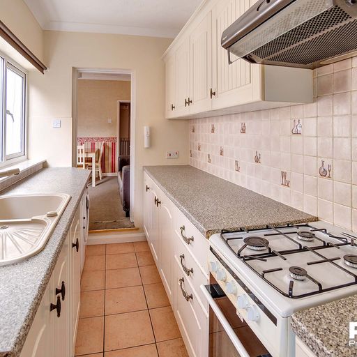 Long galley kitchen with white cabinets, grey worktop, and white goods