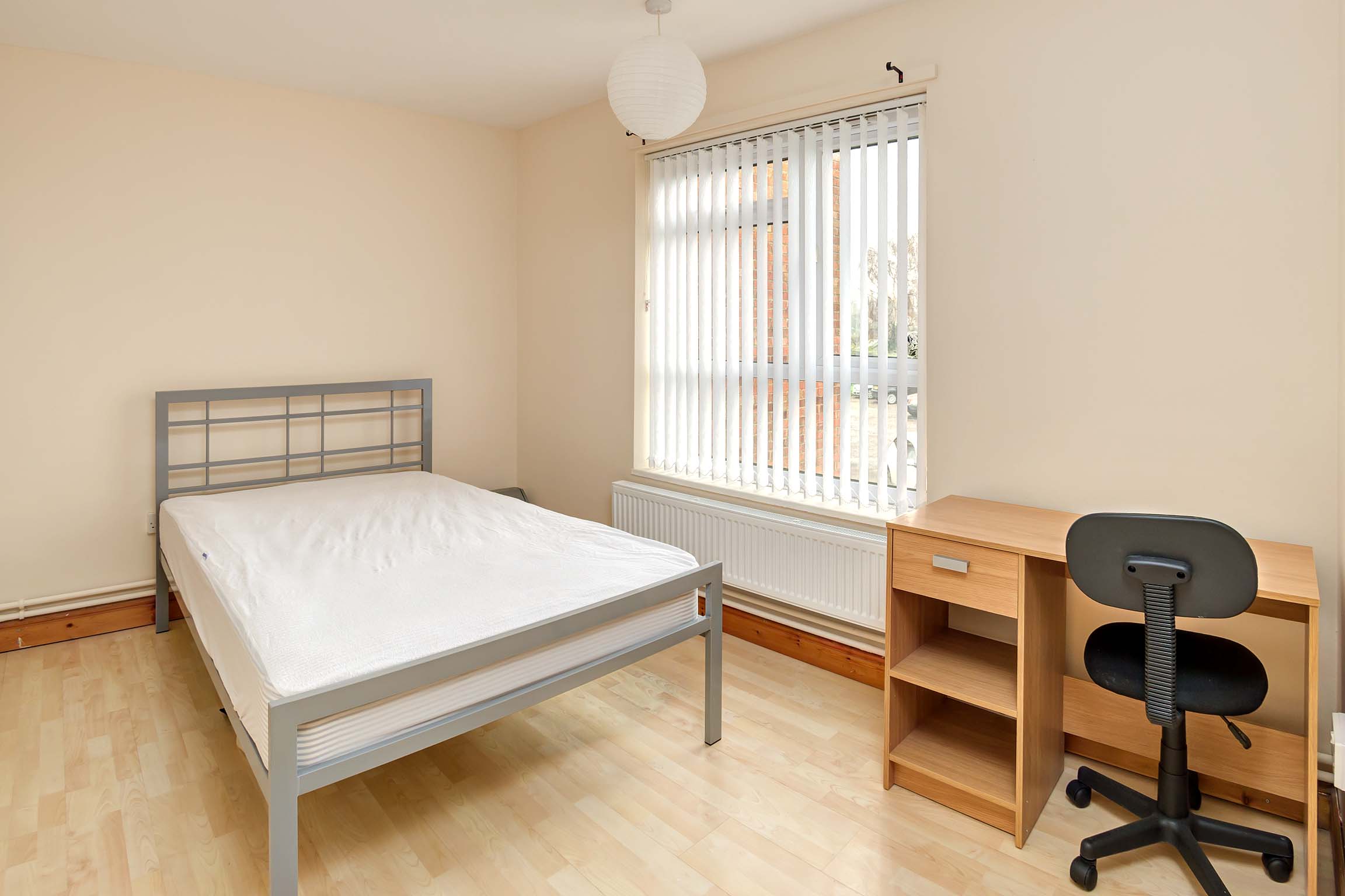 Double bedroom with wooden flooring, magnolia walls, wooden desk, metal double bed frame and white blinds up the window.