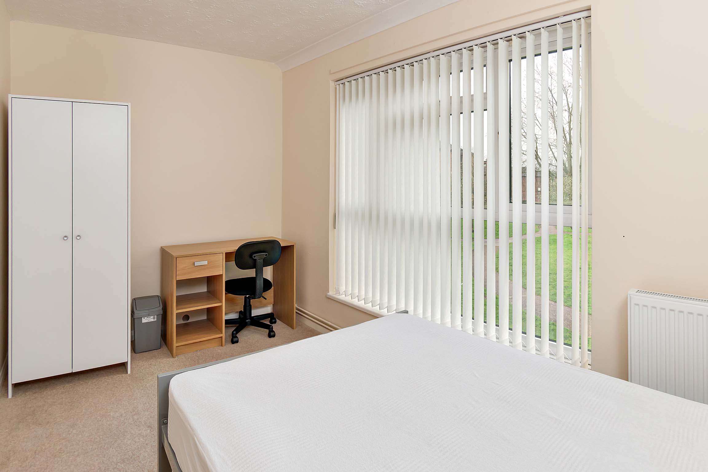 Double bedroom with large windows, a wooden desk and a white wardrobe.