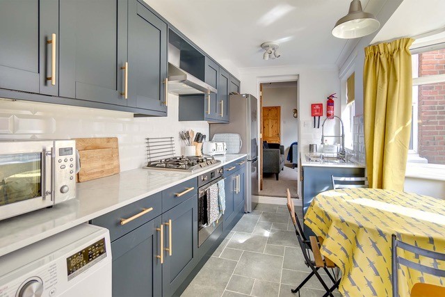 Modern galley kitchen with grey cabinets, white stone effect worktops, and round dining table