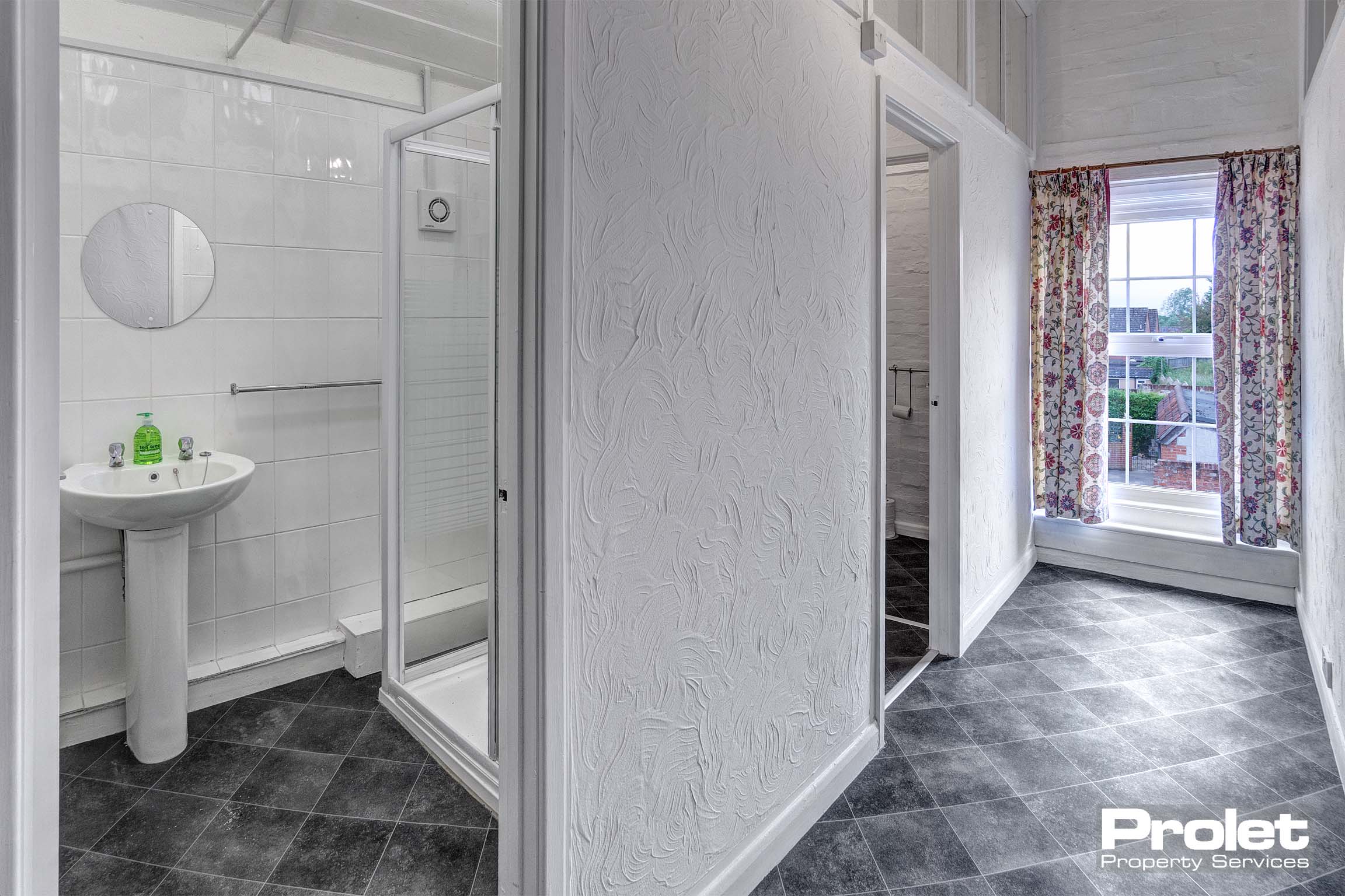 Hallway with white walls and grey vinyl flooring leading to bathroom.