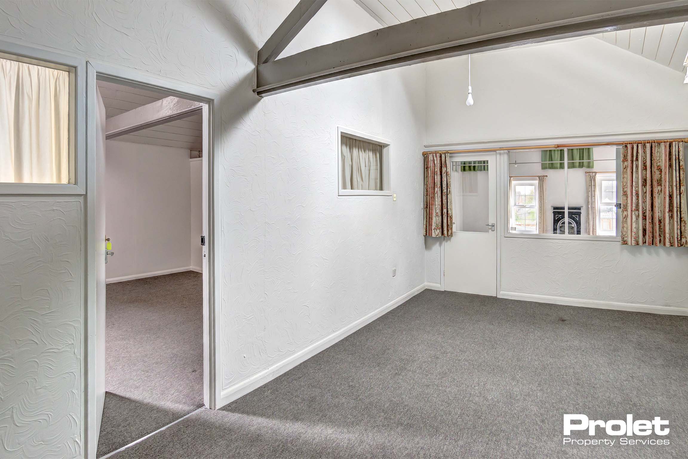 Bedroom with white walls, taupe carpet and wooden beams to ceiling. .