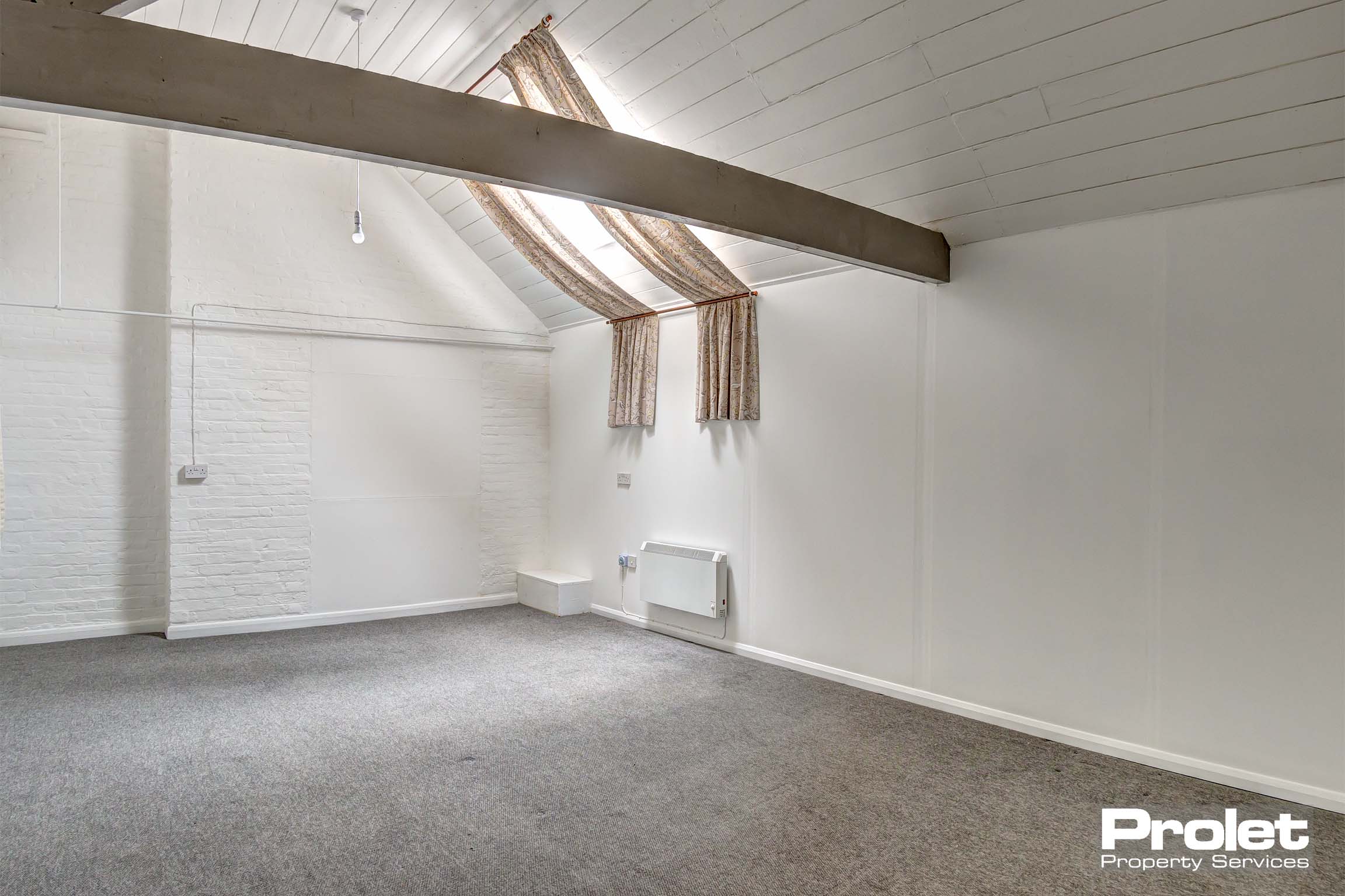 Bedroom with white walls, taupe carpet and wooden beams to ceiling.