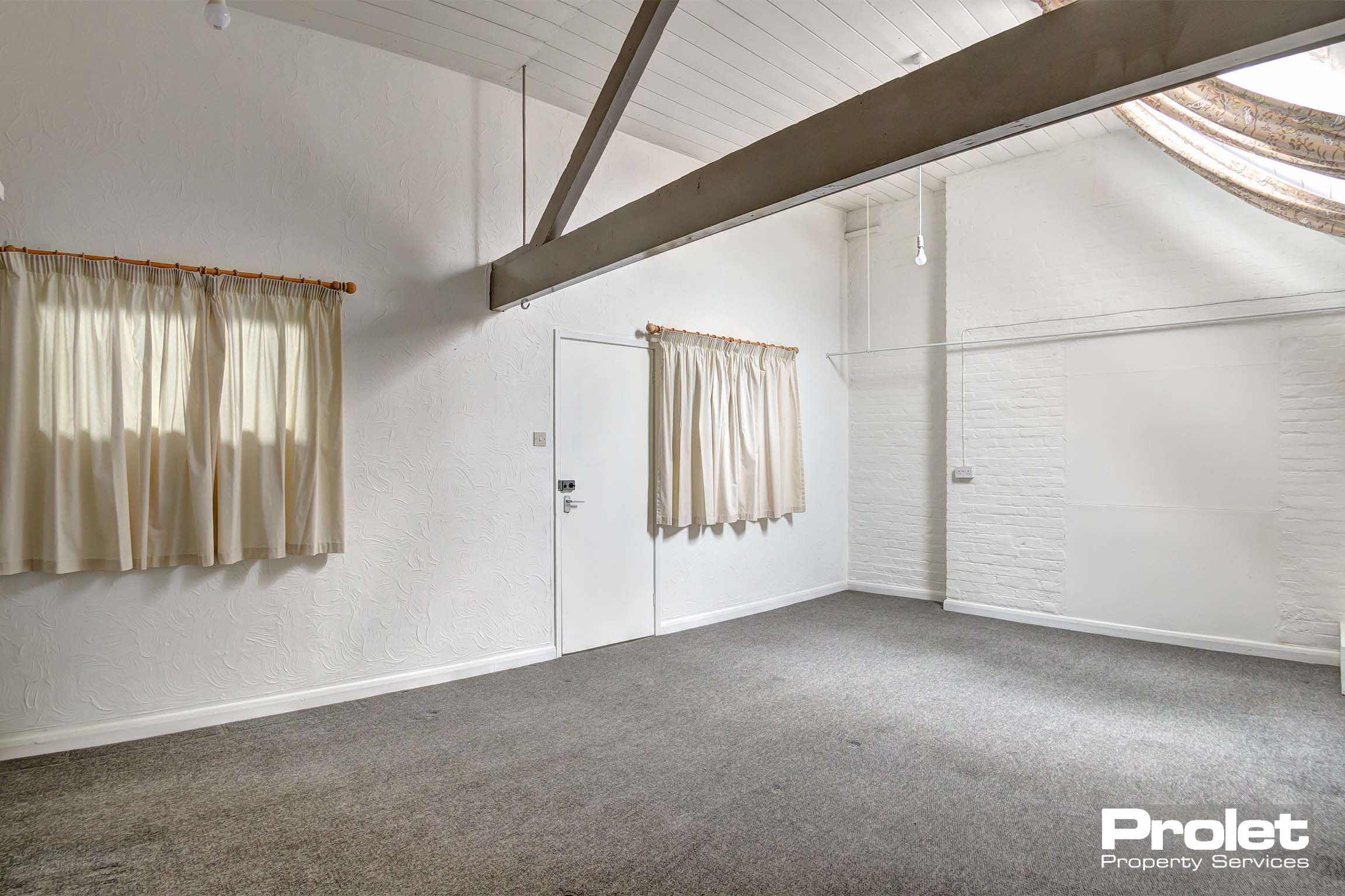 Bedroom with white walls, taupe carpet and wooden beams to ceiling.