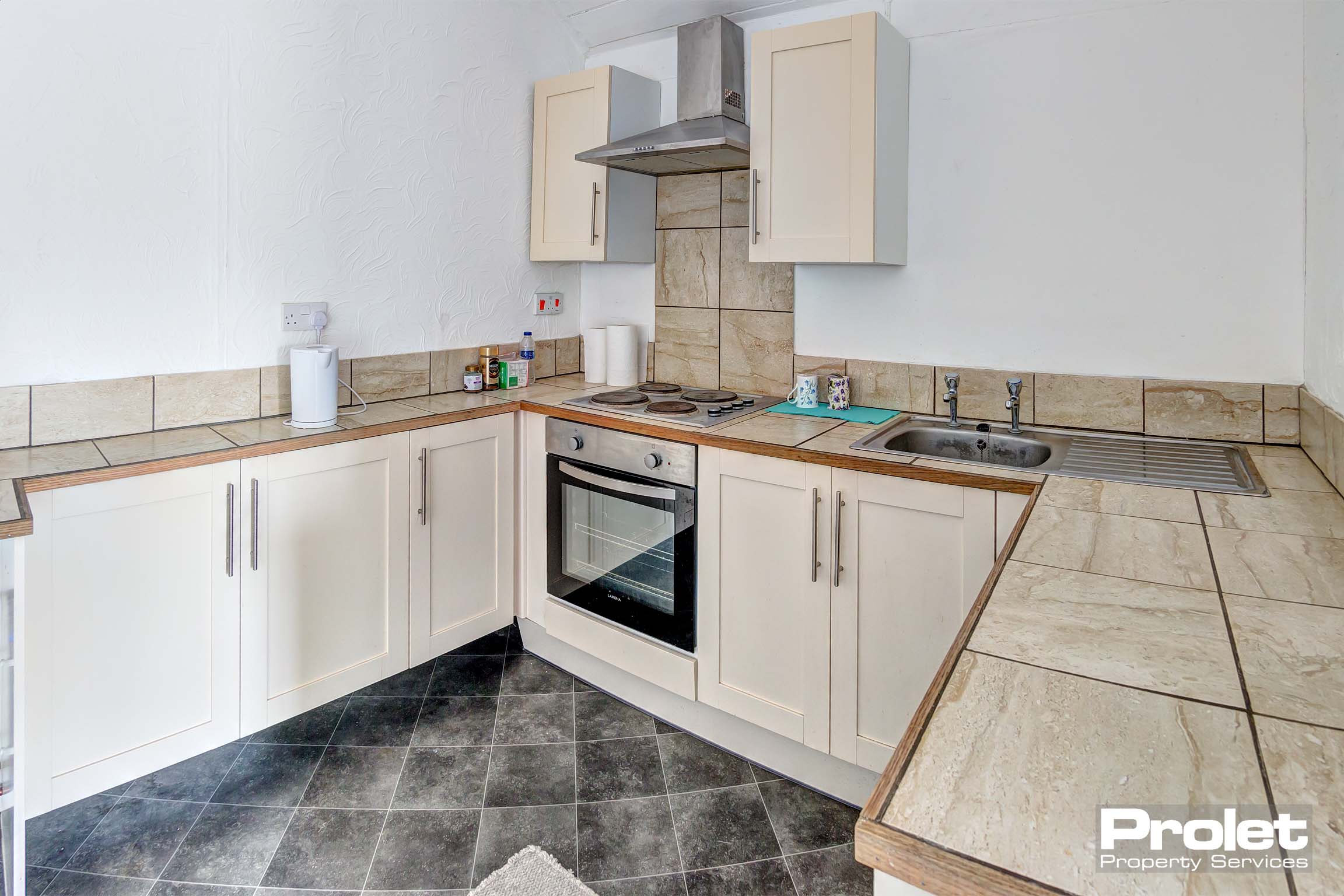 Small galley kitchen with cream cupboards and tiled worktops with electric oven.