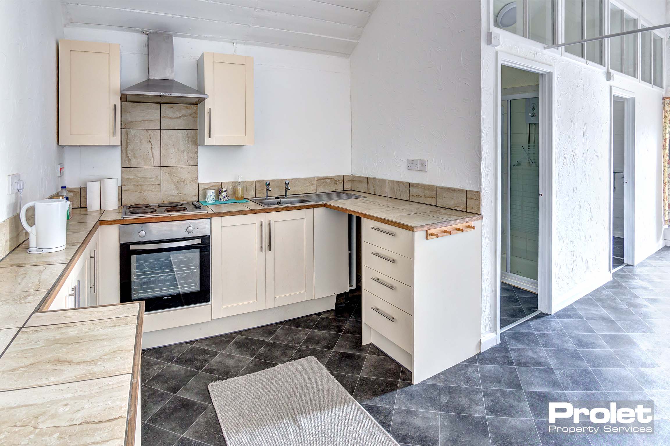 Small galley kitchen with cream cupboards and tiled worktops with electric oven.