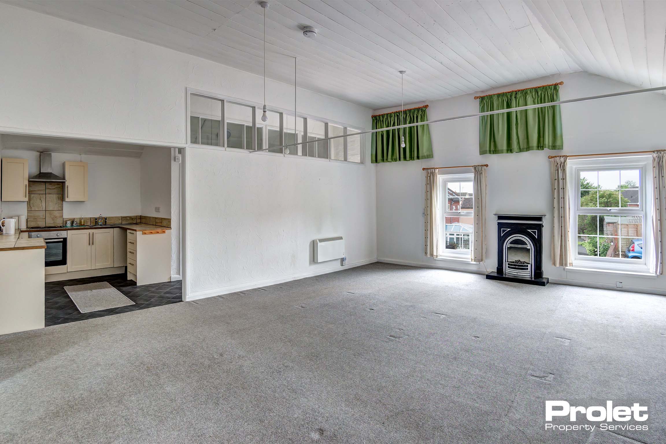 Large lounge with white walls and taupe coloured carpet. Electric fireplace.