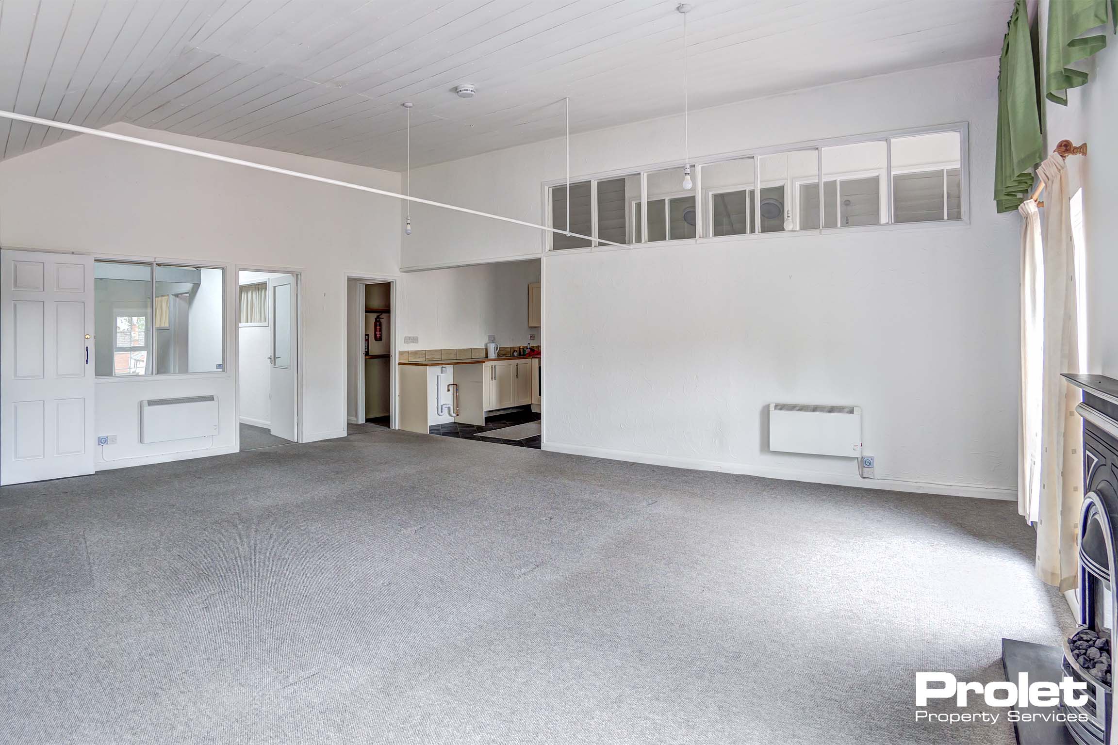 Large lounge with white walls and taupe coloured carpet. Electric fireplace.