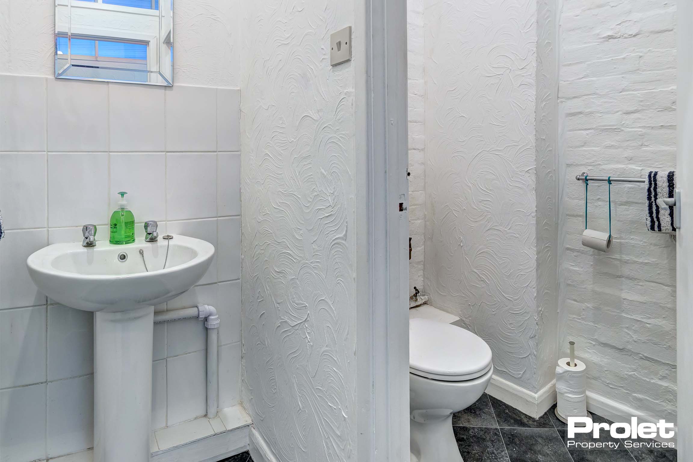 Toilet and sink with slight partition. White walls and grey vinyl floors. .