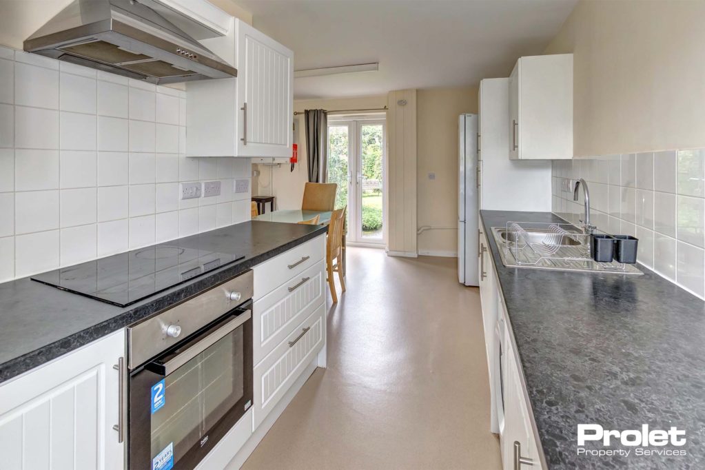 Galley style fitted kitchen with white units and dark grey worktop which opens into the dining space.