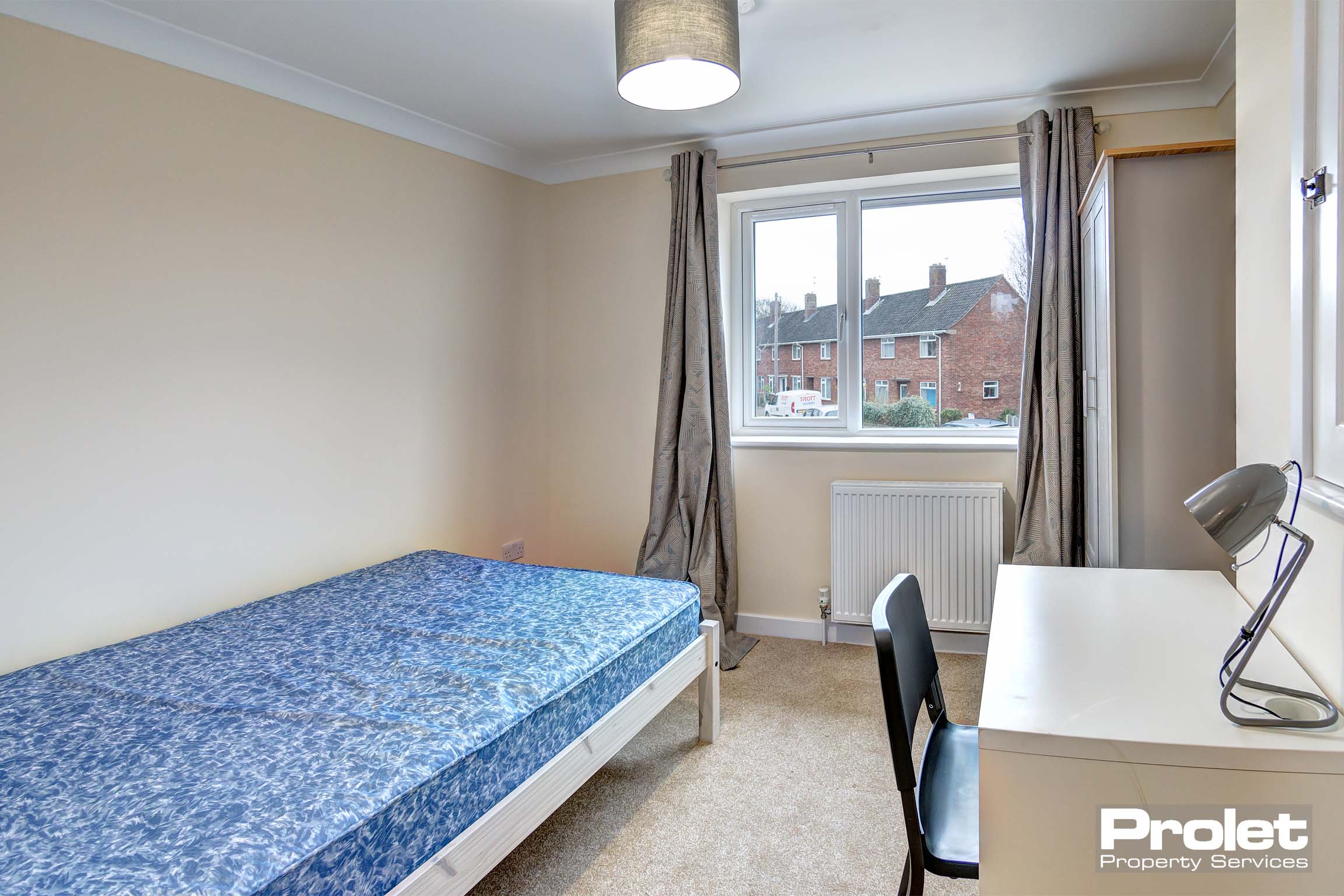 Double bedroom with neutral coloured carpet, a white desk with black chair. A door for access to the ensuite bathroom.