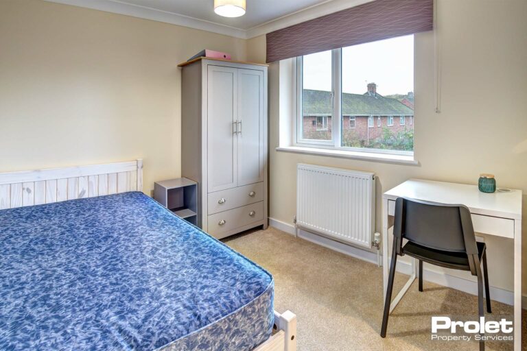 Double bedroom with neutral colour carpet, a white desk and black chair. A light grey, wooden colour wardrobe.