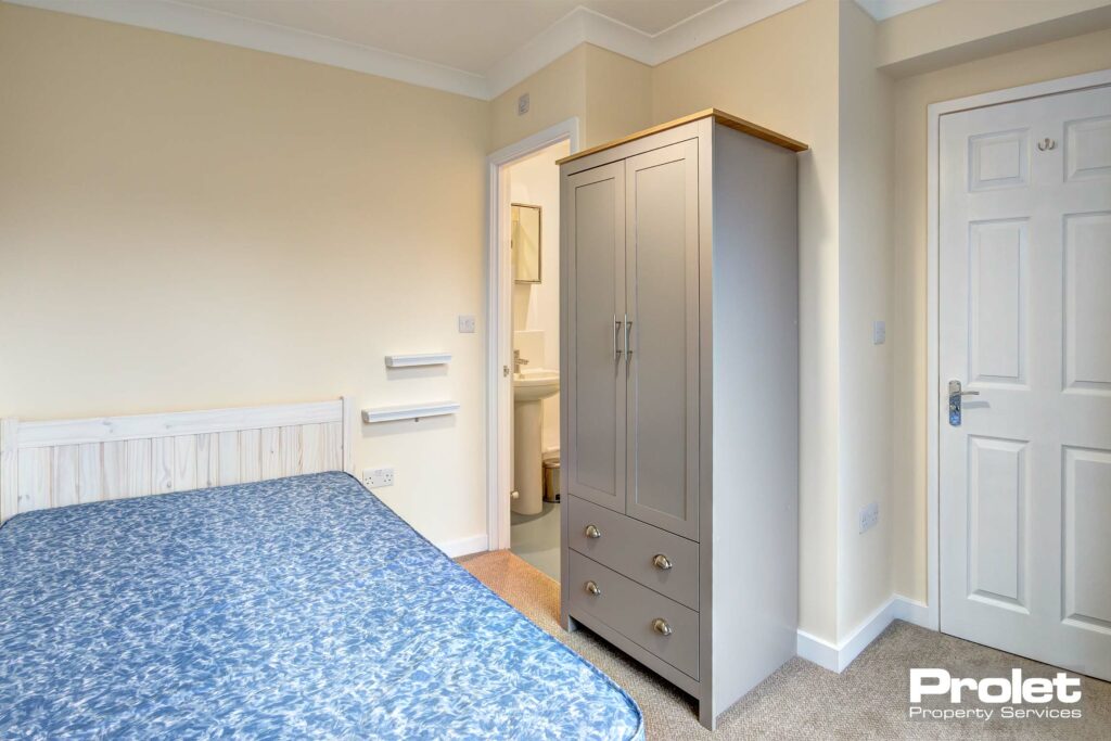 Double bedroom with grey wooden wardrobe and double bed, a white door for access to ensuite bathroom.