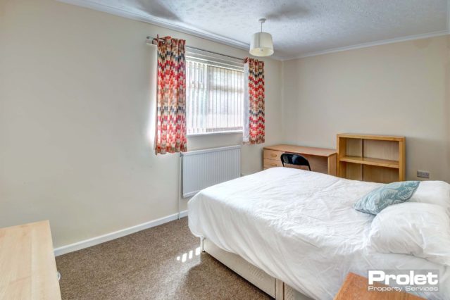 Double bedroom with multi coloured curtains, a divan bed and wooden storage units.