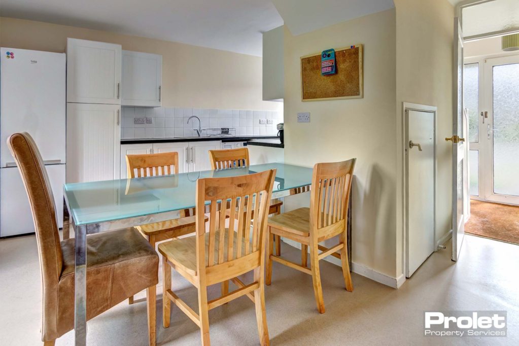 Dining area in the kitchen with glass table and wooden chairs.