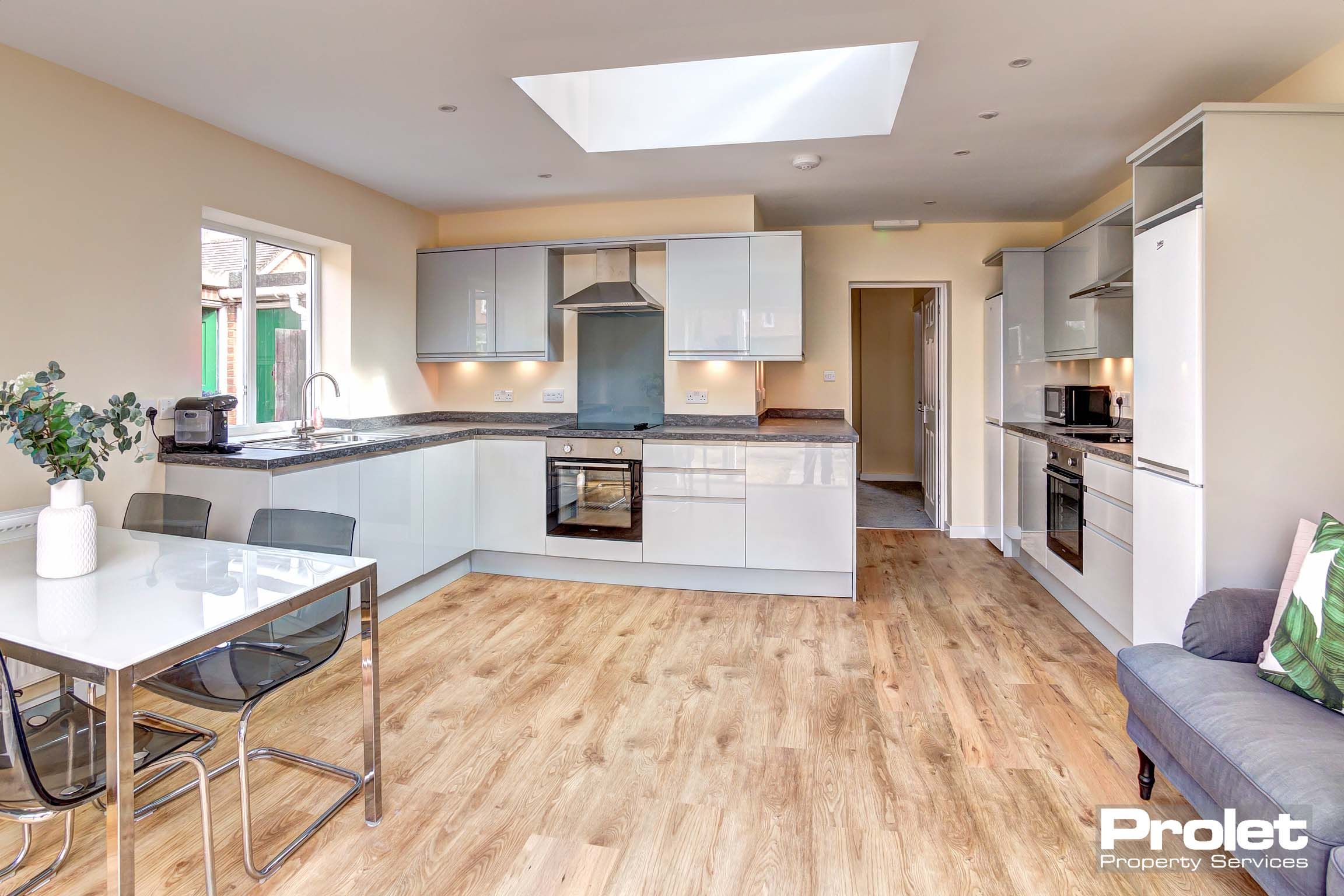 Modern kitchen with gloss white cabinets, dining table set, sofa, and white goods