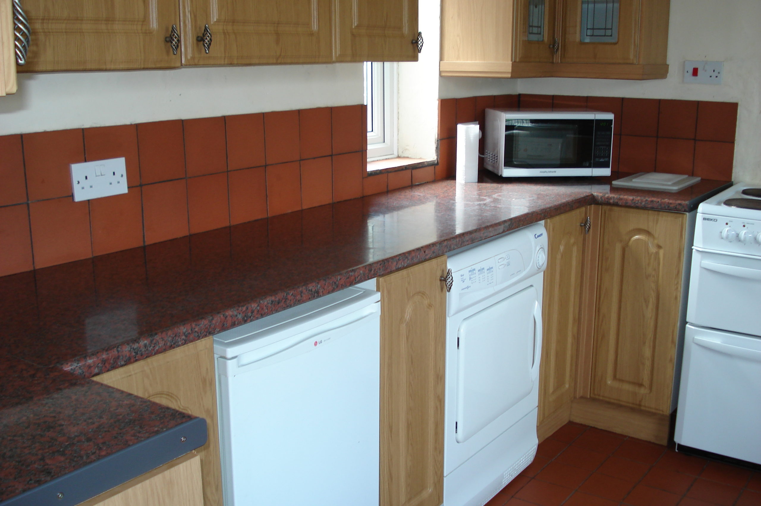 Kitchen with wooden cabinets, white goods, and tiled floor