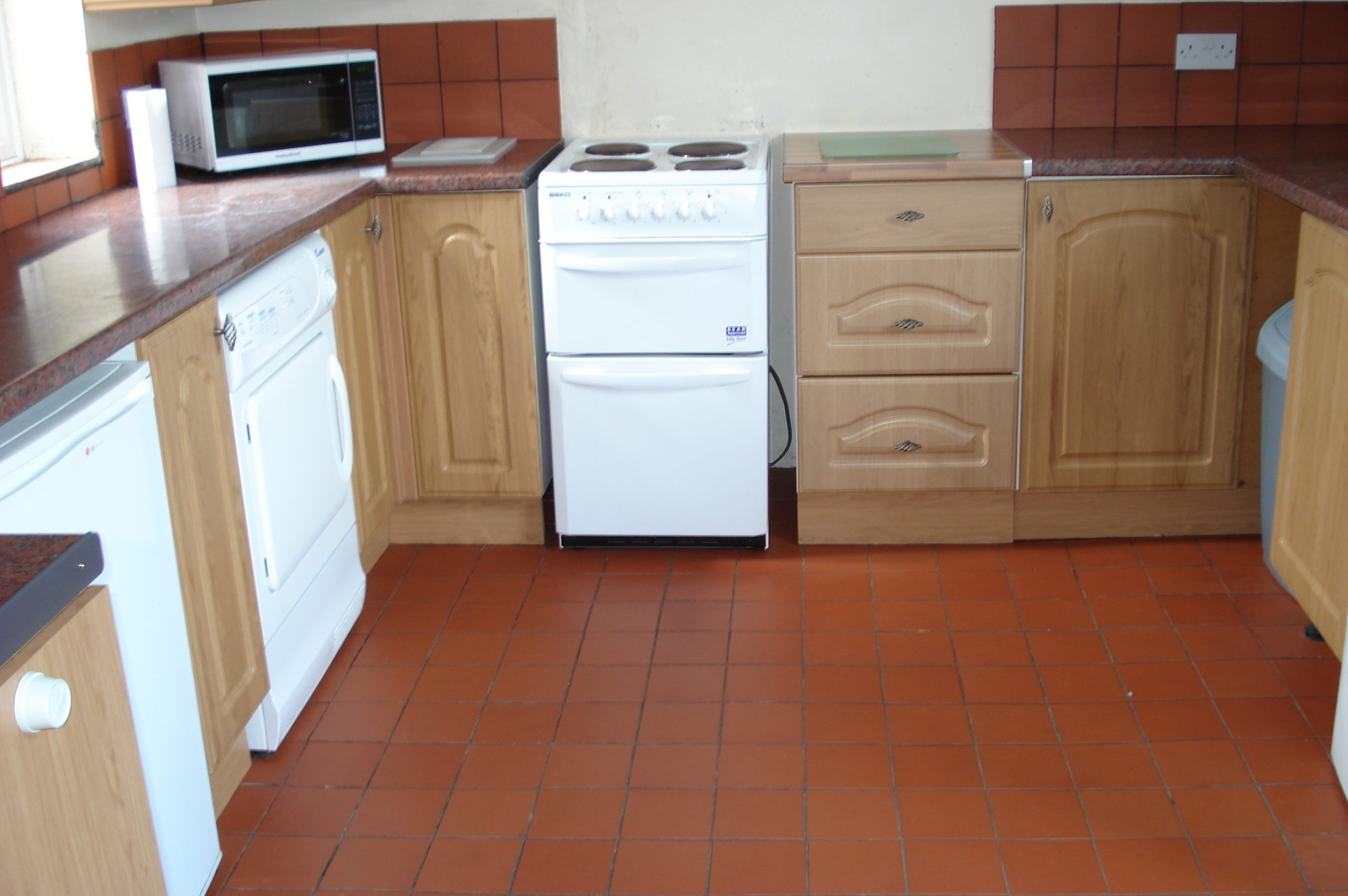 Kitchen with wooden cabinets, white goods, and tiled floor