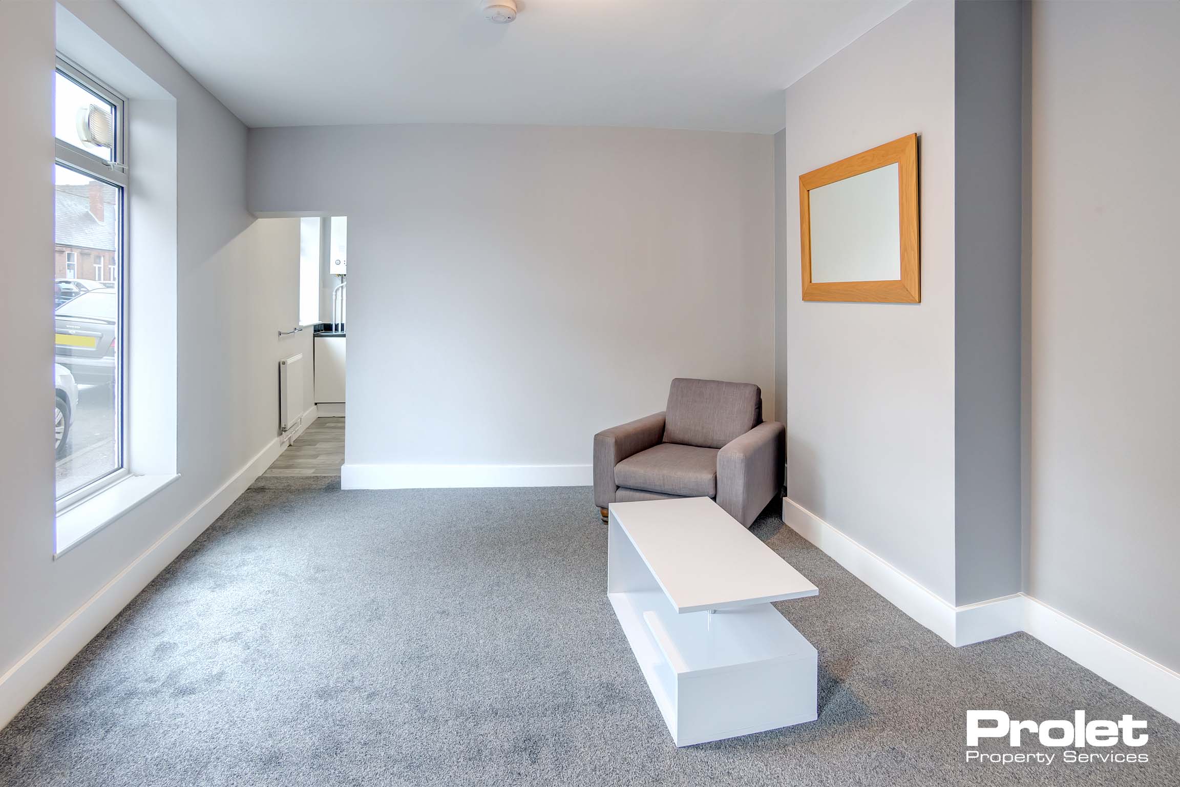 Lounge with grey carpet, and grey walls. Grey armchair and white coffee table.