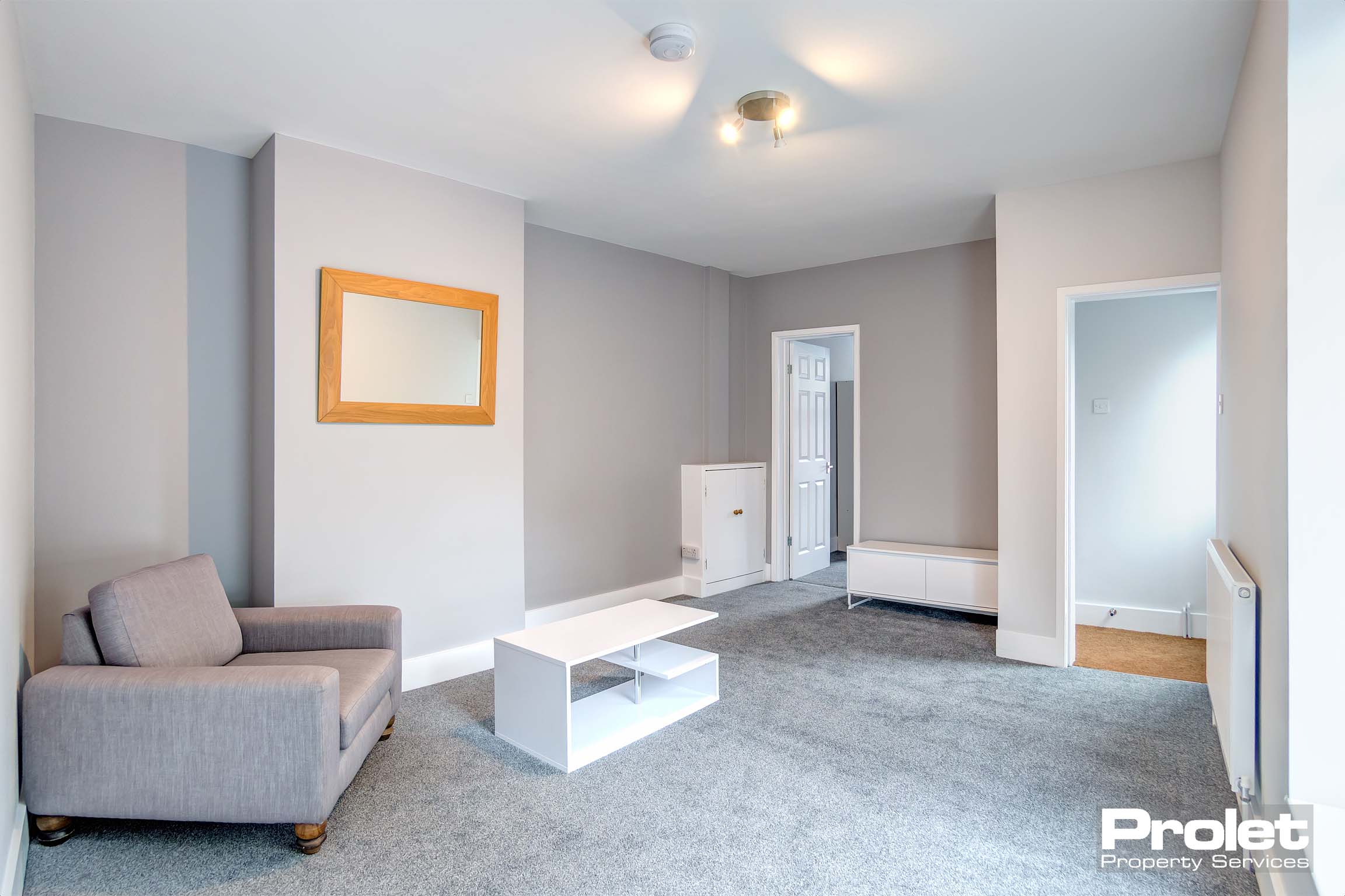 Lounge with grey carpet, and grey walls. Grey armchair and white coffee table.