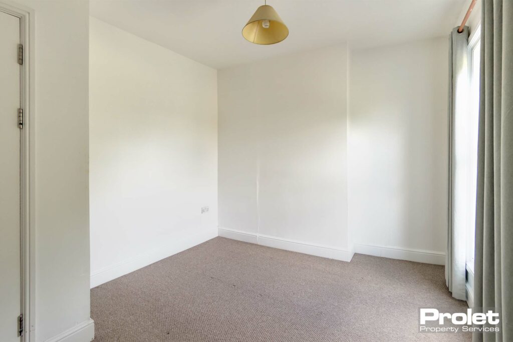 Double bedroom at front of house with white walls and light brown carpet.