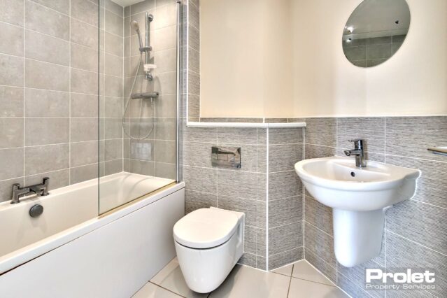 White suite with grey wall tiles and magnolia paint. Tiled floor.