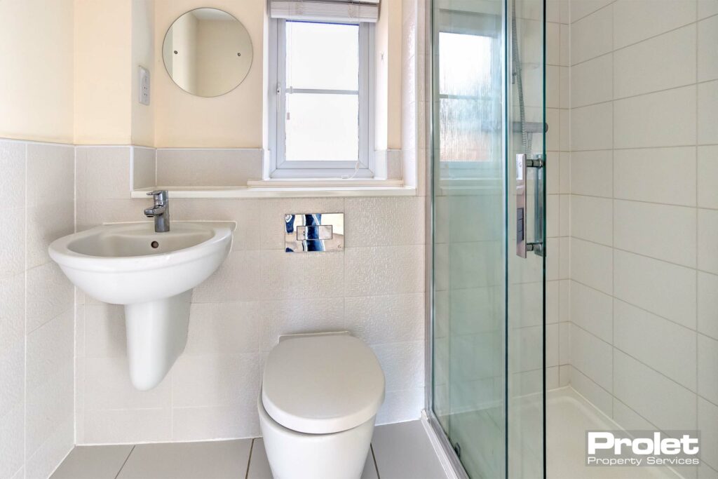 White toilet and shower cubicle with white tiles.