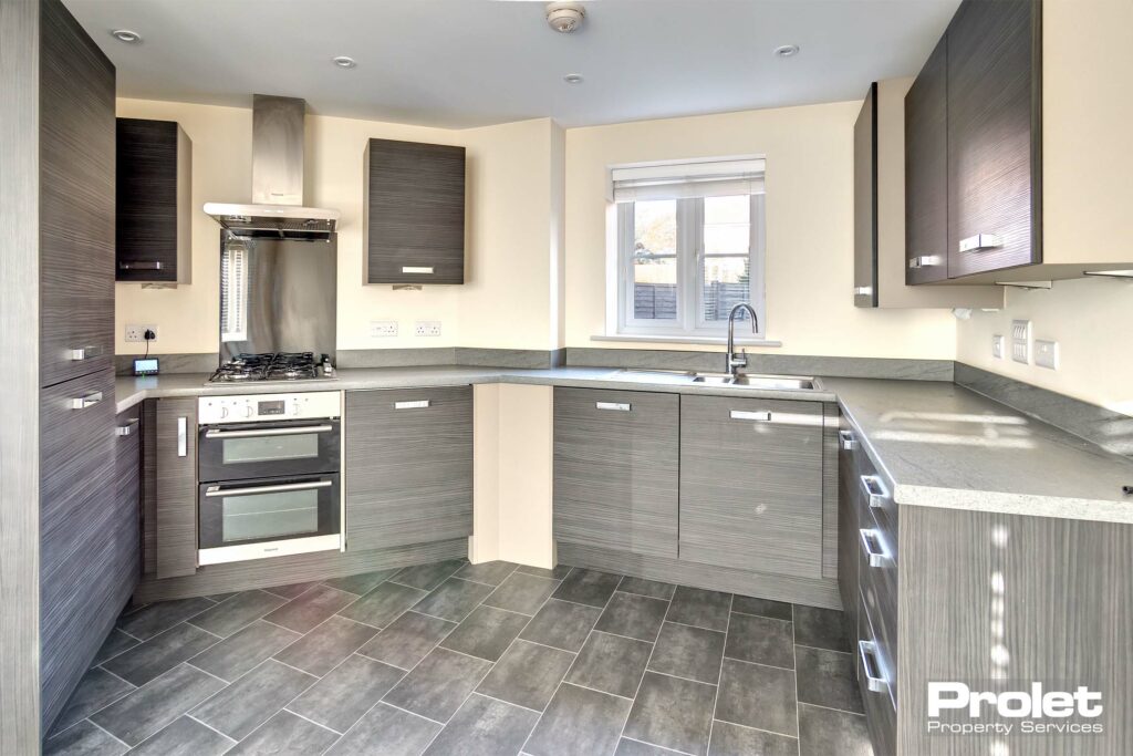 Magnolia walls with grey vinyl flooring with grey kitchen units. Oven washing machine, dishwasher and fridge freezer