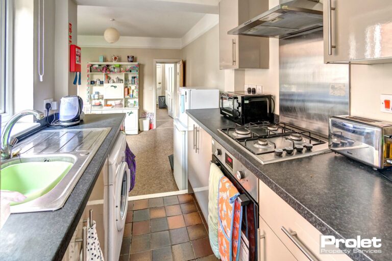 Galley style kitchen with tiled floor, hob, oven, and washing machine, leading to dining room