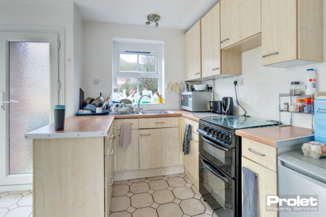 Kitchen with wood effect cupboards and counter tops, black cooker, and sink